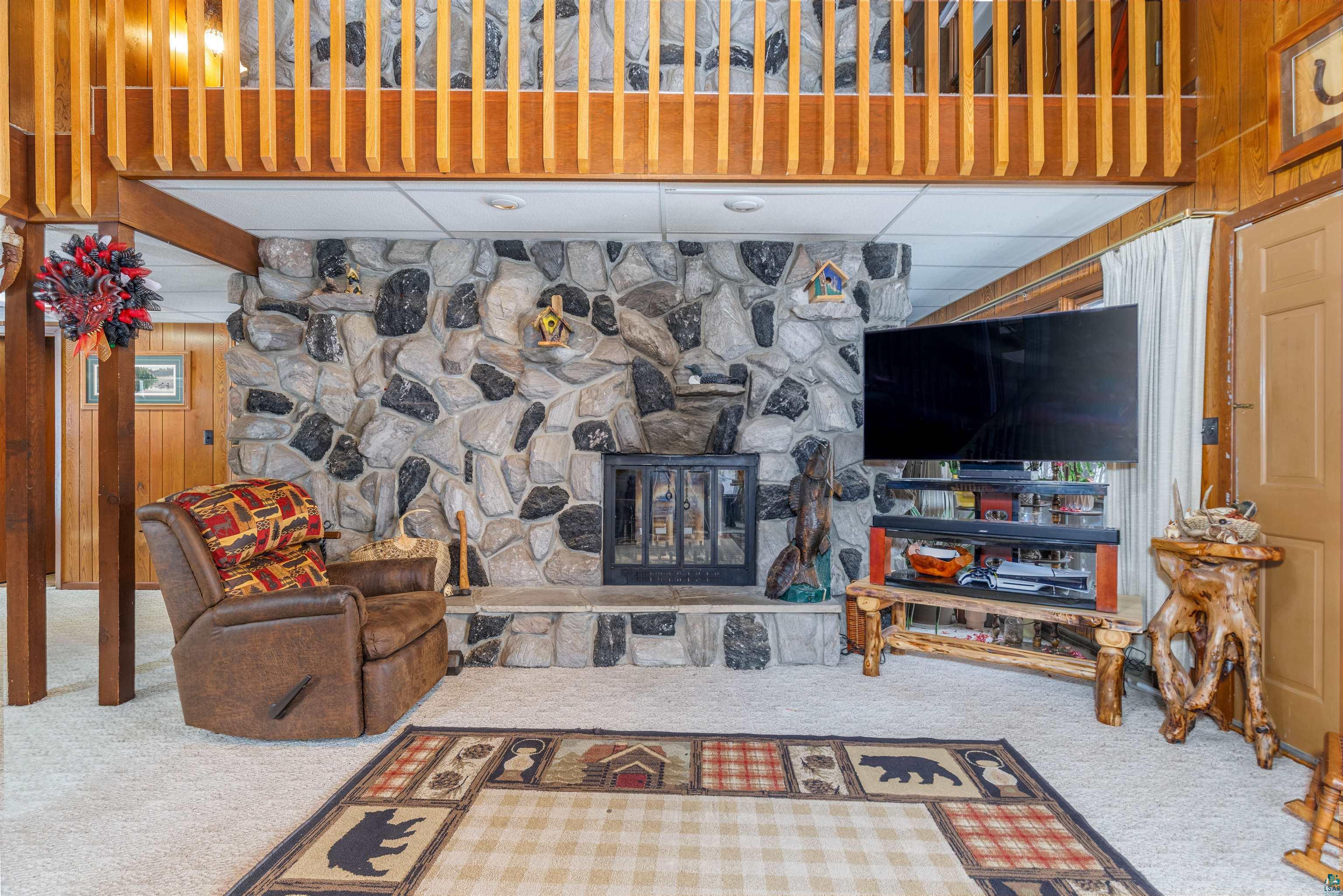 2641 Priest Point Road Ely, MN 55731 - Photo 3 of 38 Carpeted living room with a drop ceiling, a stone fireplace, and wooden walls