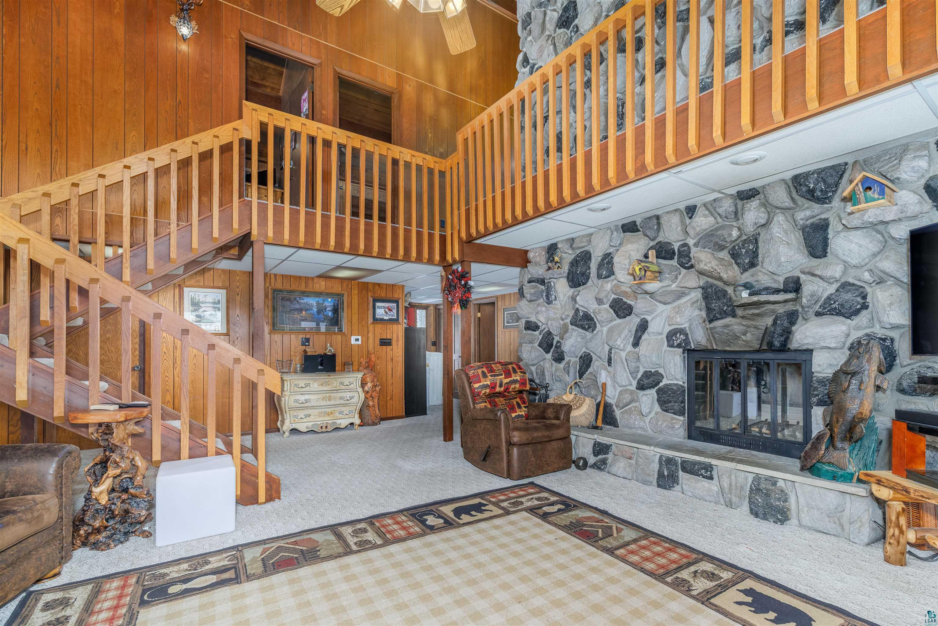 2641 Priest Point Road Ely, MN 55731 - Photo 4 of 38 Carpeted living room with wood walls, a high ceiling, ceiling fan, and a fireplace