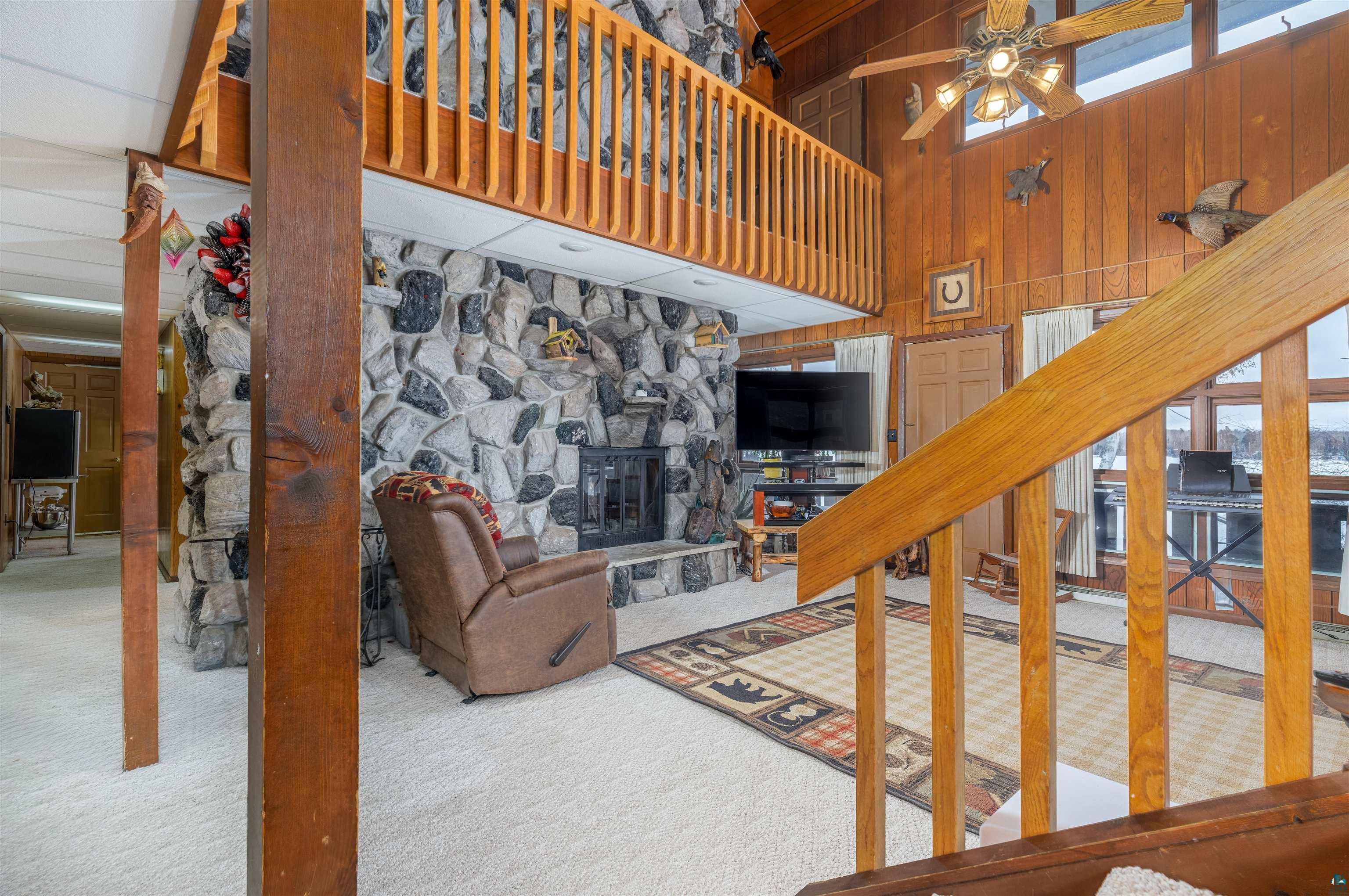 2641 Priest Point Road Ely, MN 55731 - Photo 5 of 38 Living area with a high ceiling, a fireplace, carpet floors, wooden walls, and ceiling fan