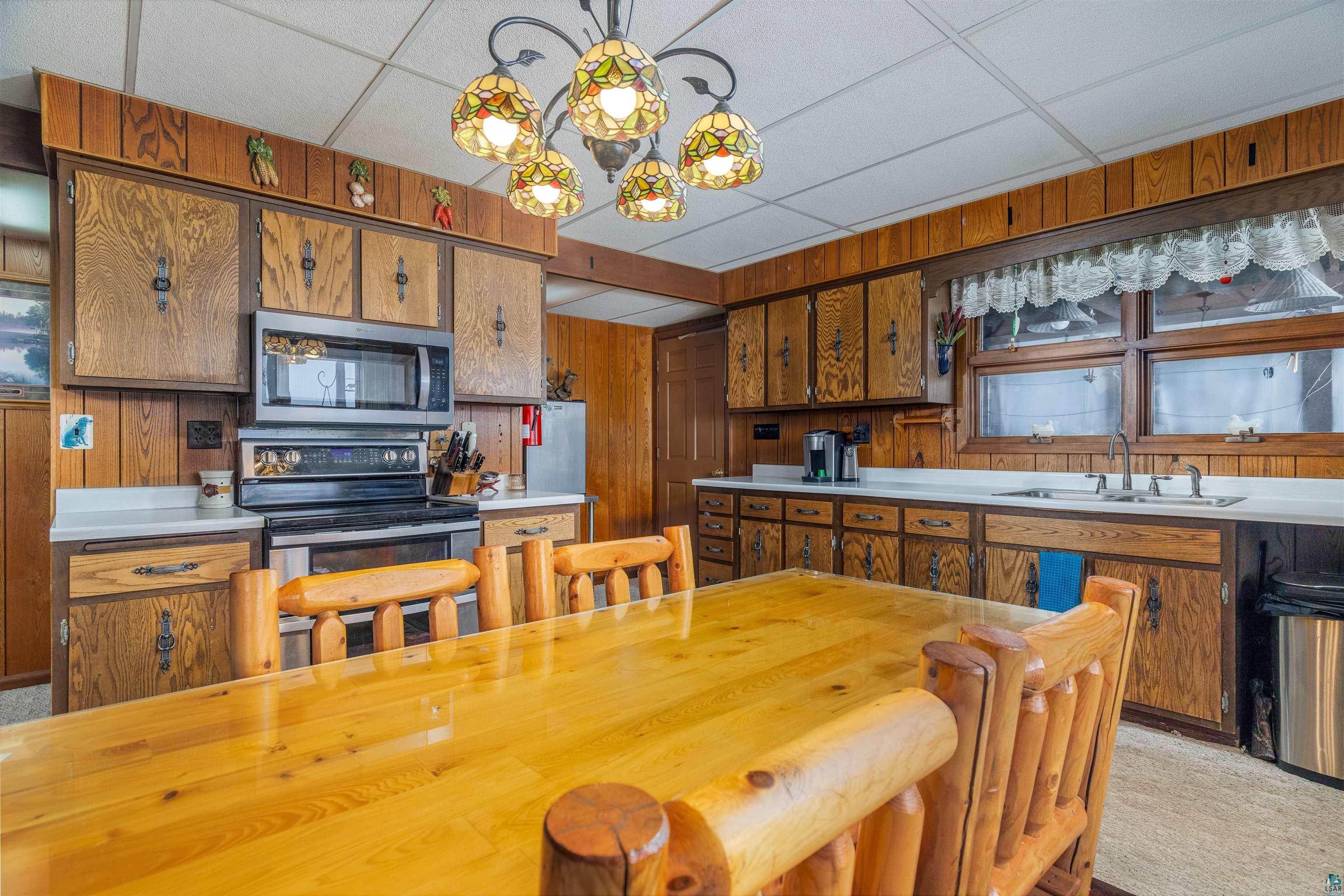 2641 Priest Point Road Ely, MN 55731 - Photo 10 of 38 Kitchen featuring wood finish cabinetry, wood walls, stainless steel appliances, a paneled ceiling, and light colored carpet