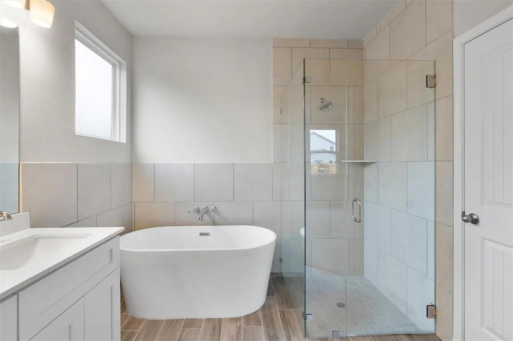332 Stellar Wind Drive Georgetown, TX 78628 - Photo 17 of 29 A well-appointed bathroom features a modern freestanding tub, a spacious glass-enclosed shower, and wood-look tile flooring.