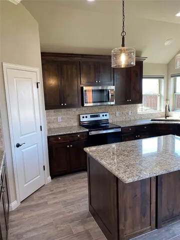 a kitchen with stainless steel appliances granite countertop wooden cabinets and a wooden floor