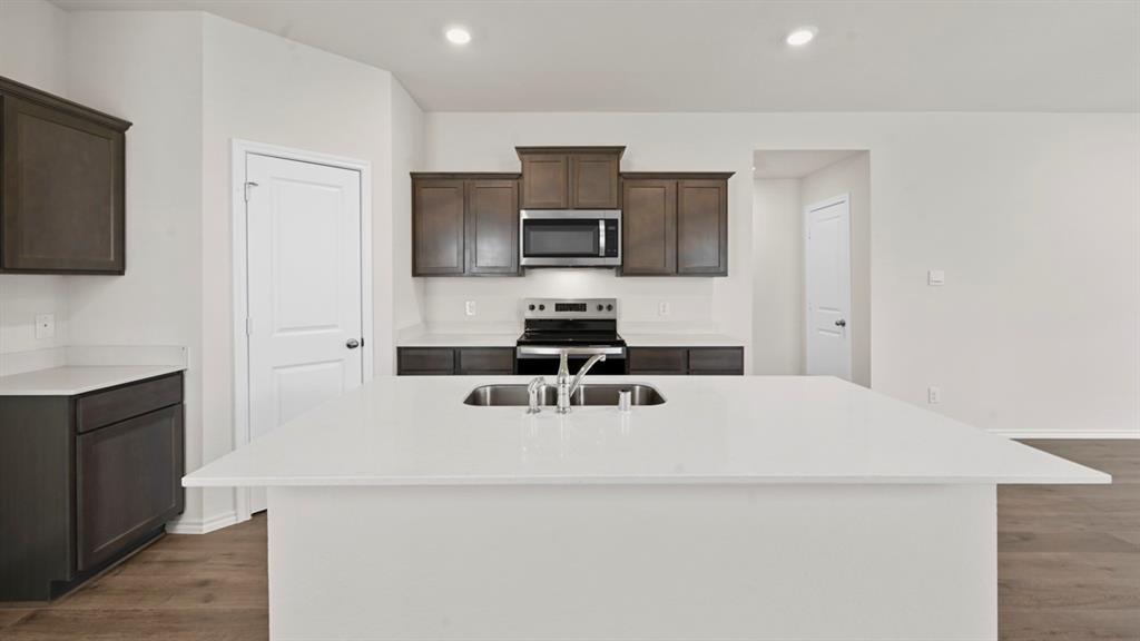 1663 Blaire Drive Tyler, TX 75704 - Photo 2 of 26 Kitchen featuring a large island with an undermount sink, white countertops, dark wood-finish cabinetry, and stainless steel appliances