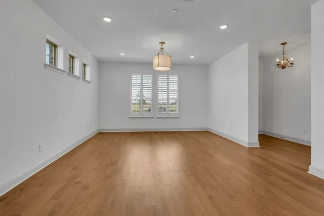 an empty room with wooden floor chandelier and windows