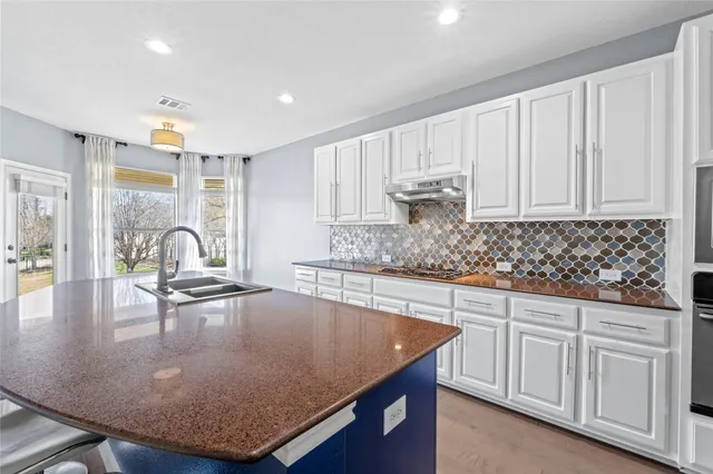 a kitchen with kitchen island granite countertop a sink a stove cabinets and living room view