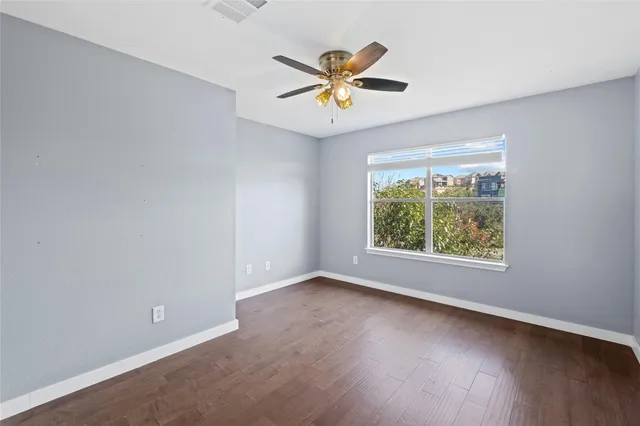 an empty room with wooden floor chandelier fan and windows