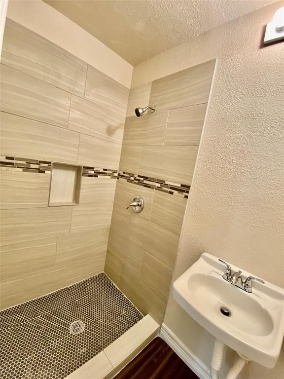 6716 Sjolander Road Baytown, TX 77521 - Photo 12 of 26 Second bathroom featuring a walk-in shower with beige tiling and a decorative mosaic accent strip. It includes a small white pedestal sink with chrome fixtures and a built-in niche for shower essentials. The floor of the shower has a black and white pebble tile design.