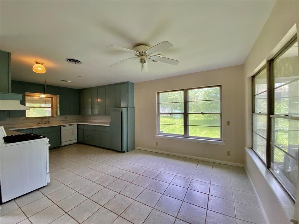 6716 Sjolander Road Baytown, TX 77521 - Photo 13 of 26 The kitchen with ample natural light, featuring tile flooring, green cabinetry, and a ceiling fan. It includes a window over the sink and a large window on the side wall, providing a view of the greenery outside.