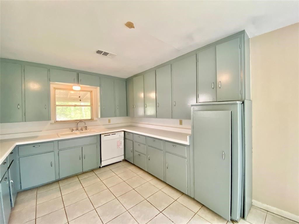 6716 Sjolander Road Baytown, TX 77521 - Photo 15 of 26 This kitchen features light blue cabinetry with ample storage, tile flooring, a window above the sink providing natural light, and includes a white dishwasher and a full-sized refrigerator.