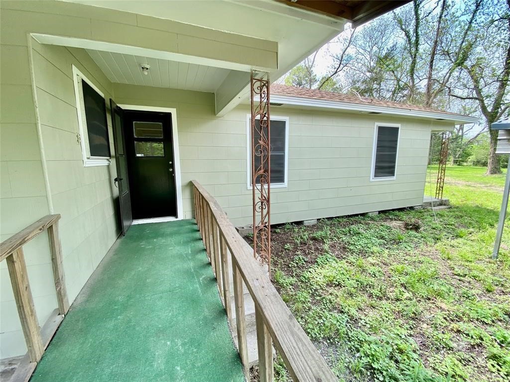 6716 Sjolander Road Baytown, TX 77521 - Photo 18 of 26 One-story home featuring a covered entryway, green carpeted porch with wooden railings, and a view of the yard with mature trees.