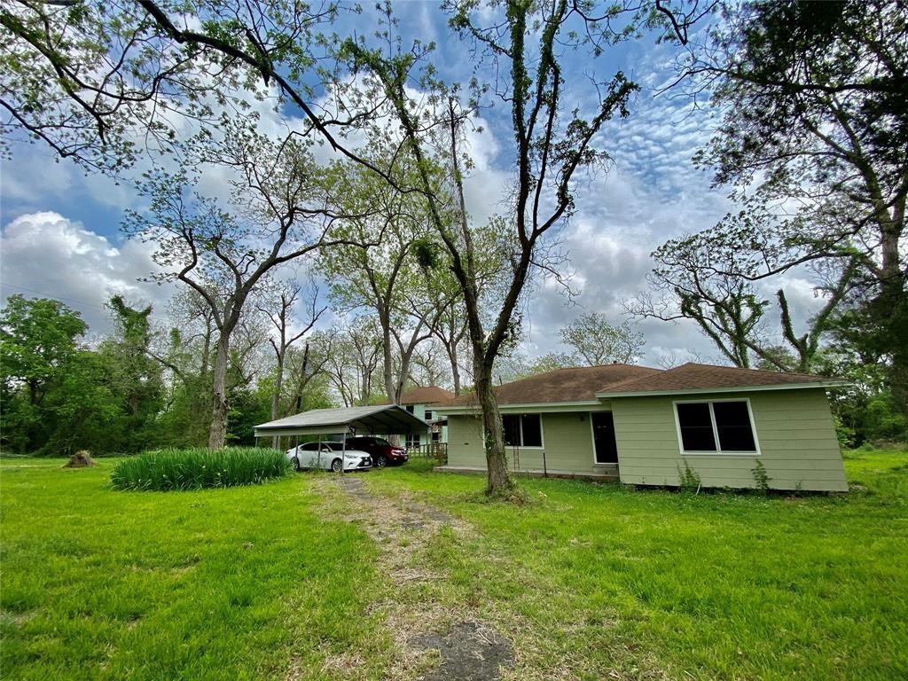 6716 Sjolander Road Baytown, TX 77521 - Photo 5 of 26 One-story home with a green exterior and white trim, featuring a carport on the left side. The property is surrounded by mature trees and has ample green yard space.