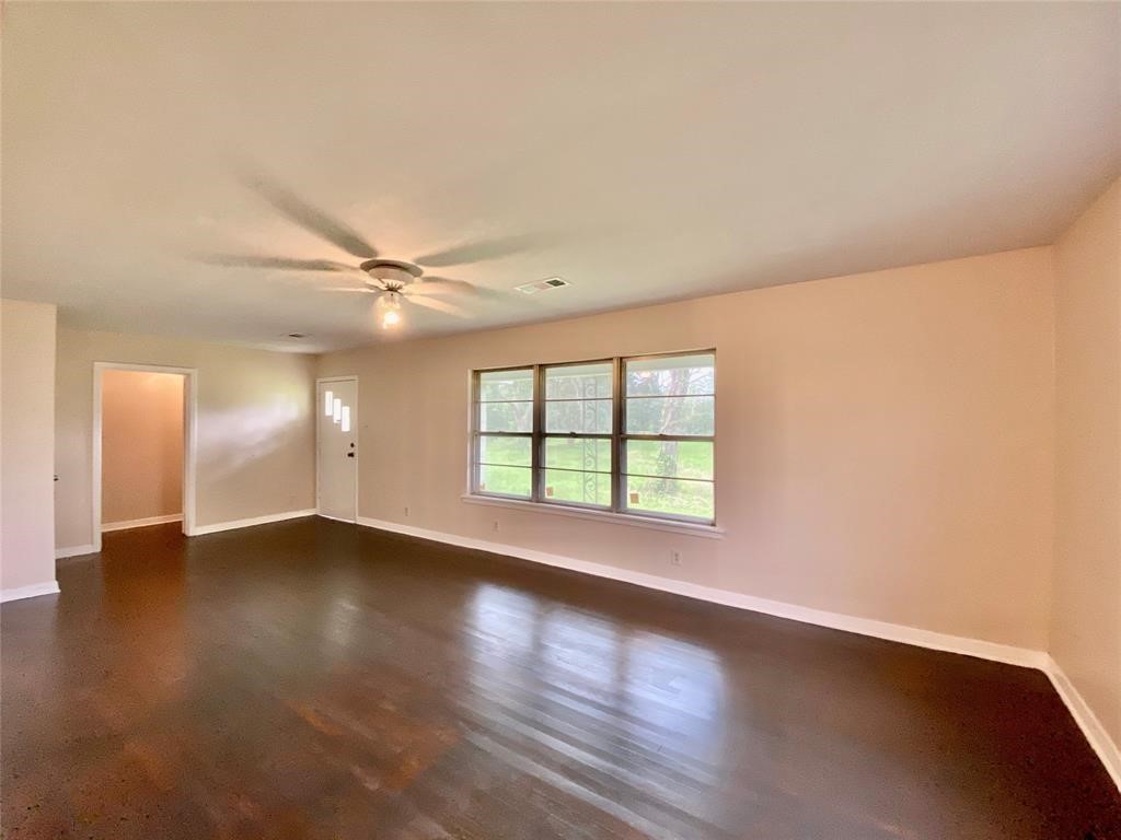 6716 Sjolander Road Baytown, TX 77521 - Photo 6 of 26 A bright, spacious living room with hardwood floors, neutral paint, and a large window allowing for ample natural light. It features a ceiling fan and offers a clean, blank canvas for personalization.