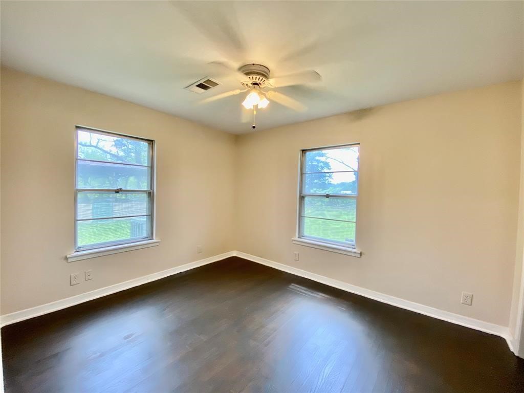 6716 Sjolander Road Baytown, TX 77521 - Photo 10 of 26 Bedroom features neutral walls, dark hardwood floors, two large windows providing ample natural light, and a ceiling fan. It appears spacious and well-lit, ideal for a variety of layouts.
