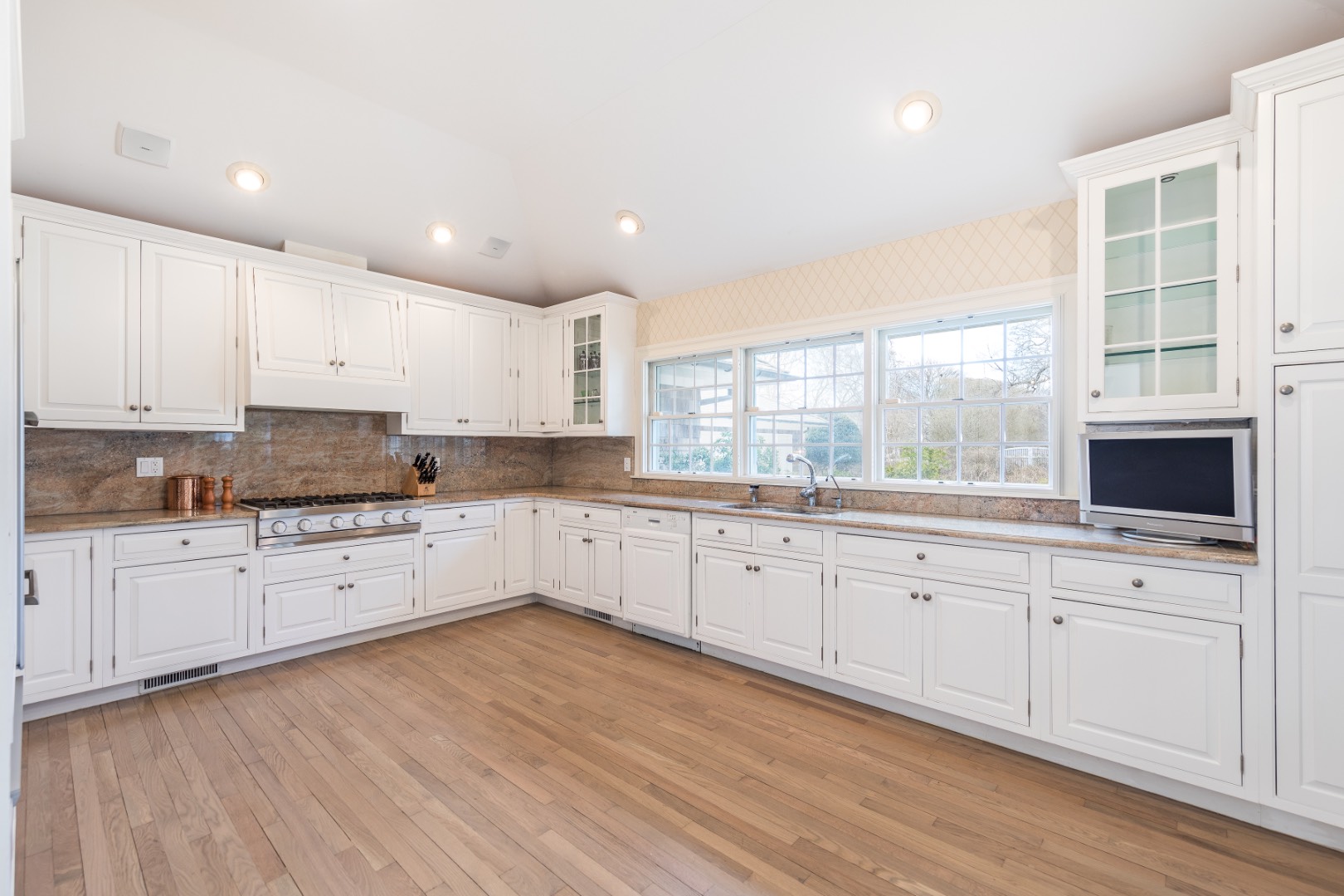 16 Amy's Lane East Hampton, NY 11937 - Photo 6 of 17 a large kitchen with granite countertop a stove top oven a sink and white cabinets with wooden floor