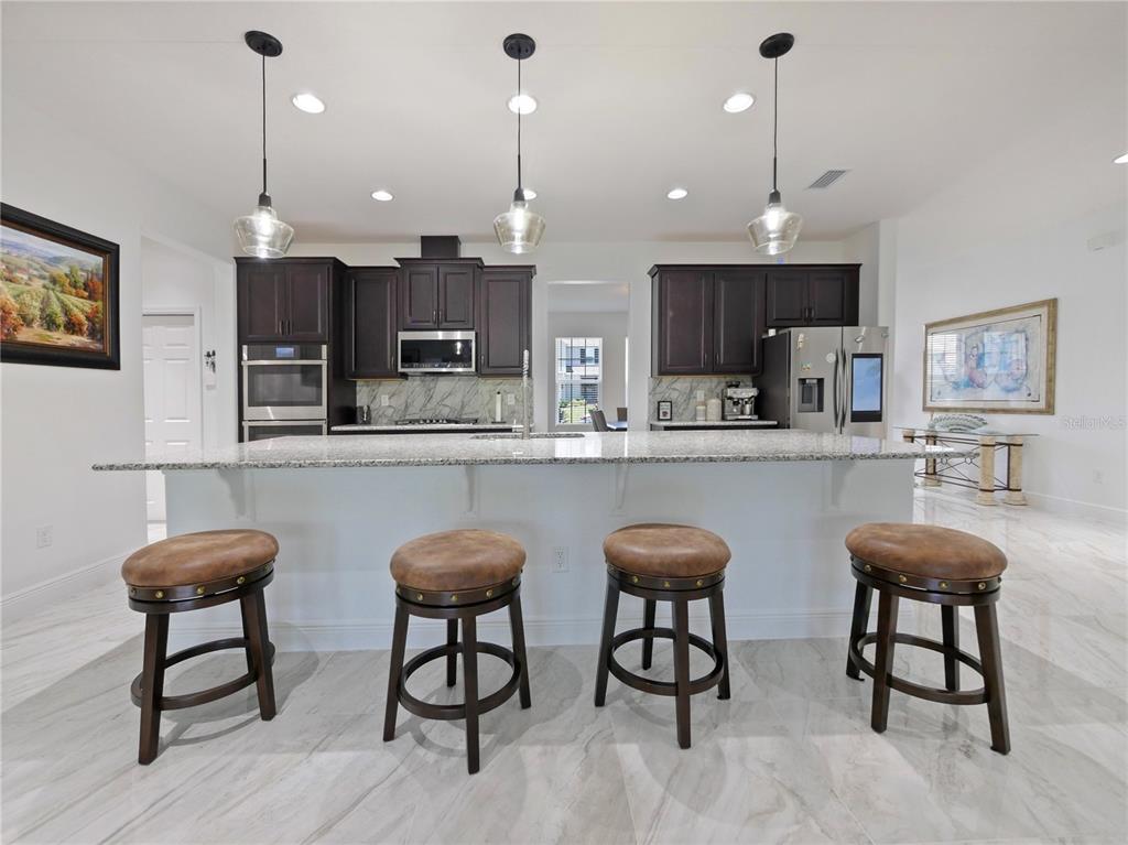 5264 Obsidian Gate Road Mount Dora, FL 32757 - Photo 14 of 49 a kitchen with stainless steel appliances kitchen island granite countertop a dining table chairs sink and white cabinets