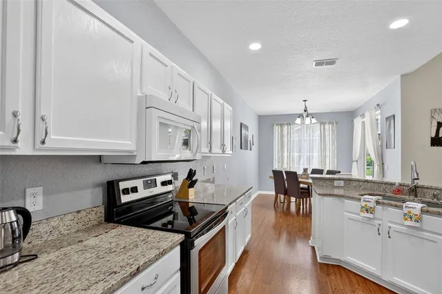 a kitchen with stainless steel appliances granite countertop a stove top oven a sink a dining table and chairs with wooden floor