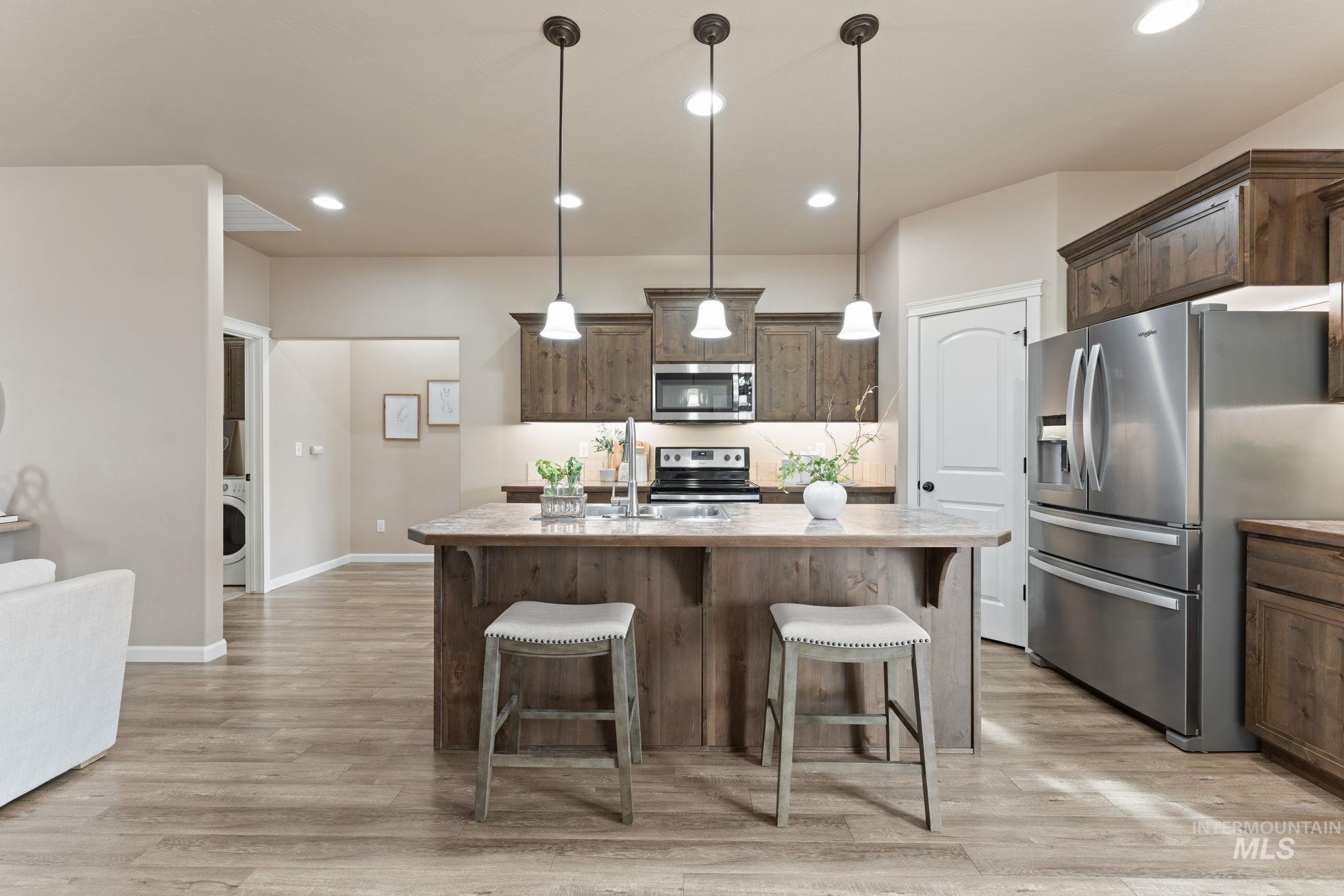 1001 13th Street Rupert, ID 83350 - Photo 12 of 40 Kitchen featuring stainless steel appliances, dark wood finish cabinets, a kitchen breakfast bar, a kitchen island with sink, and light wood-style floors