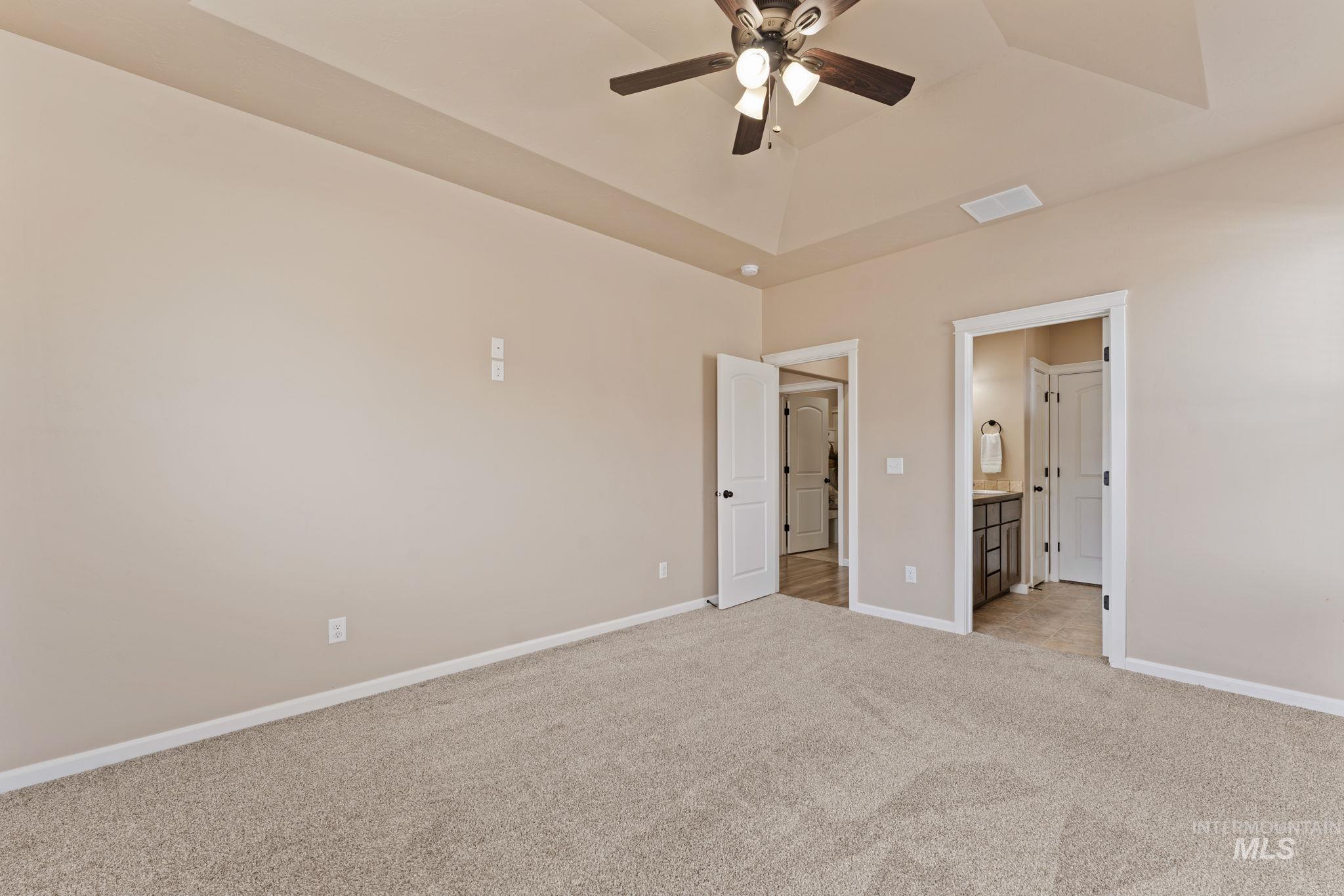 1001 13th Street Rupert, ID 83350 - Photo 15 of 40 Unfurnished bedroom with light carpet, connected bathroom, a ceiling fan, and a raised ceiling
