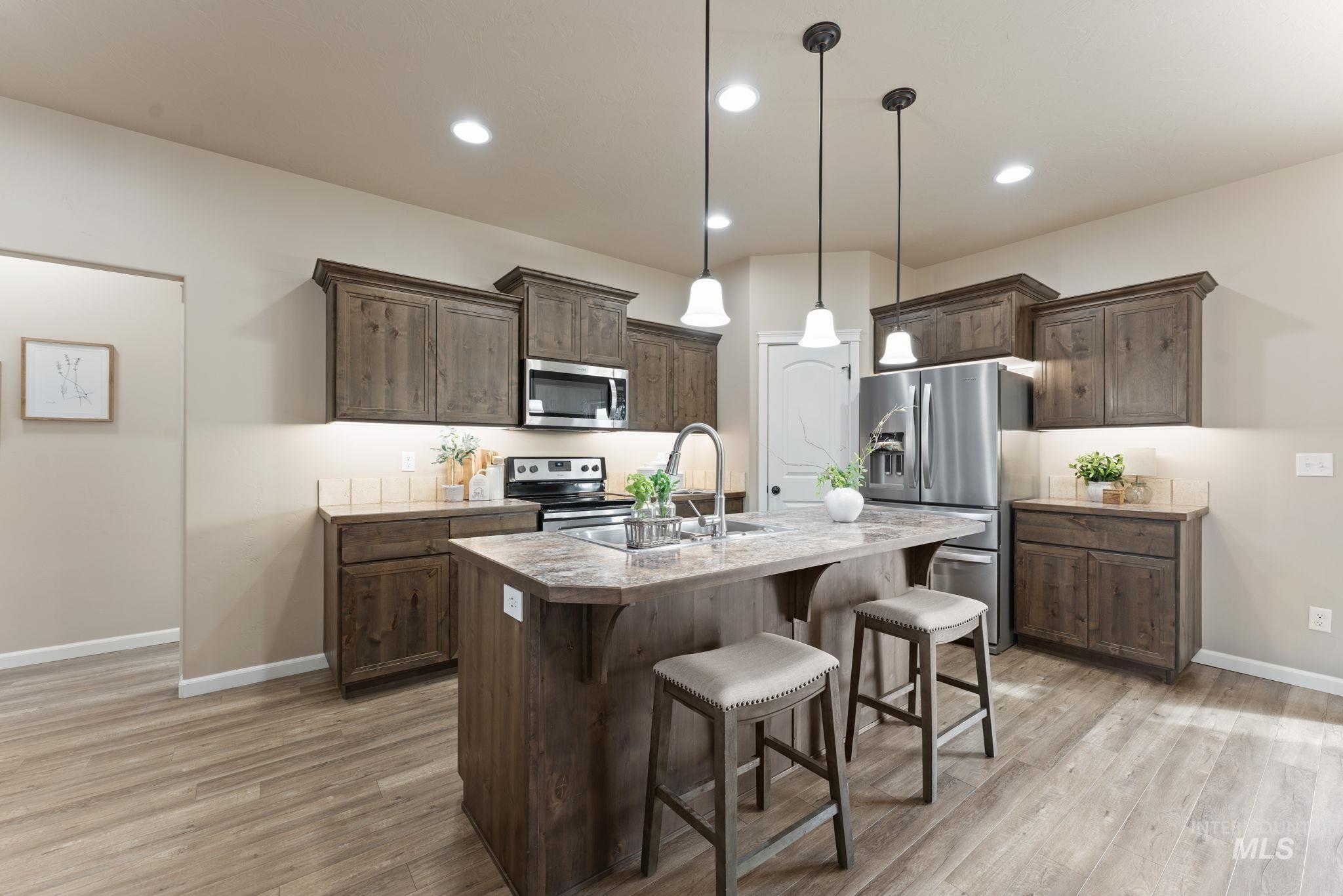 1001 13th Street Rupert, ID 83350 - Photo 8 of 40 Kitchen with a breakfast bar area, stainless steel appliances, light countertops, dark wood finish cabinets, and an island with sink