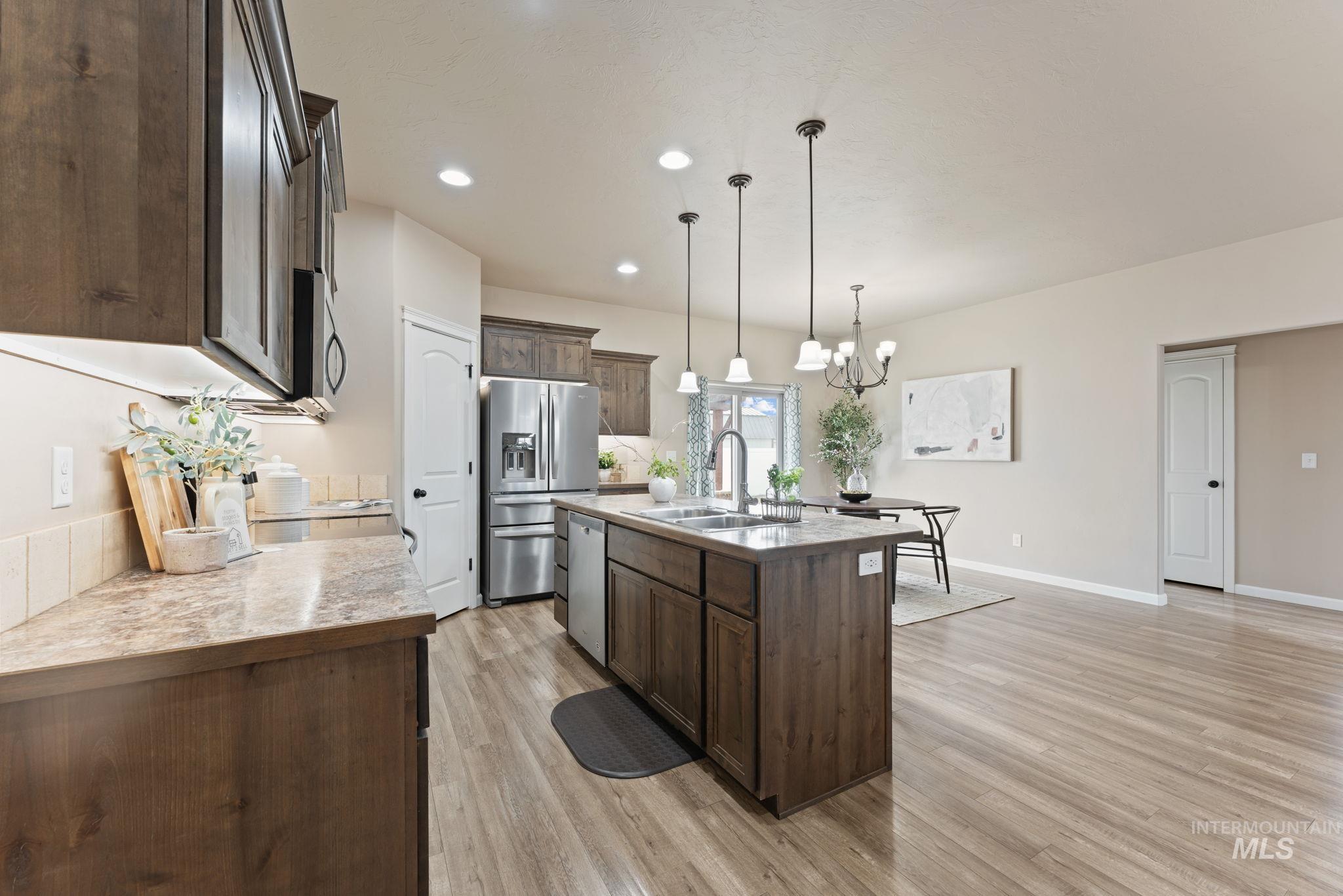 1001 13th Street Rupert, ID 83350 - Photo 9 of 40 Kitchen with dark wood finish cabinets, stainless steel appliances, a center island with sink, suspended lighting, and light wood-type flooring