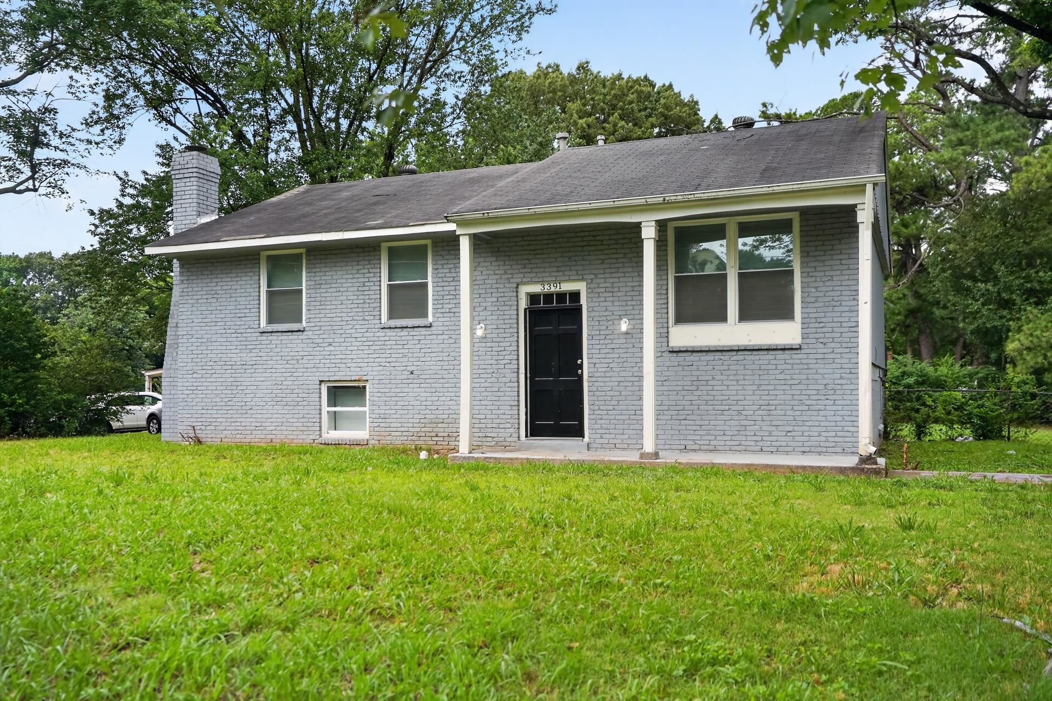 Grey brick exterior with a black front door, featuring a covered entry porch supported by white columns