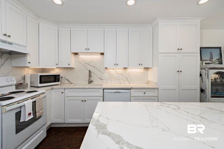 Kitchen featuring white appliances, white cabinetry, recessed lighting, light stone counters, and decorative backsplash