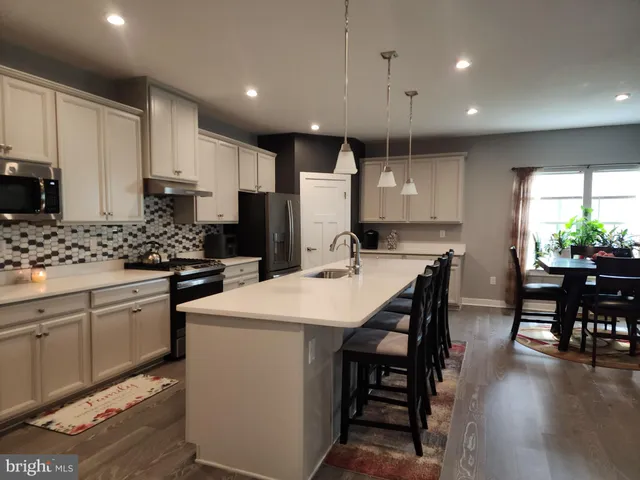 a kitchen with kitchen island a stove a refrigerator a dining table and chairs with wooden floor