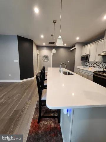 a kitchen with stainless steel appliances kitchen island granite countertop a stove top oven a sink a refrigerator and white cabinets with wooden floor