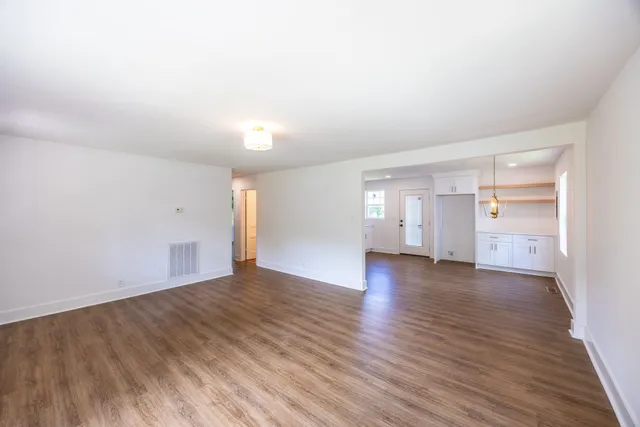 a view of empty room with wooden floor and kitchen