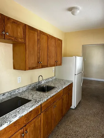 a kitchen with granite countertop a sink a stove and a refrigerator with wooden cabinets