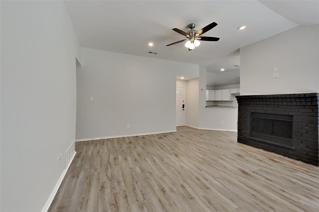 7809 Meadowlark Lane Rowlett, TX 75088 - Photo 4 of 18 an empty room with wooden floor a ceiling fan a fireplace and a ceiling fan