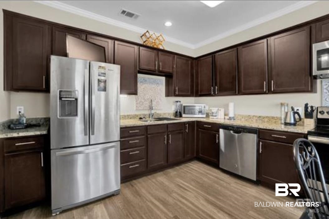 430 West Fort Morgan Road Gulf Shores, AL 36542 - Photo 23 of 27 Kitchen featuring wood-finish flooring, dark wood cabinetry, light-toned countertops, a stainless steel refrigerator, and a stainless steel dishwasher