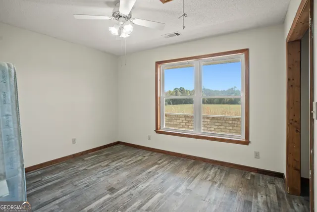 an empty room with wooden floor ceiling fan and windows