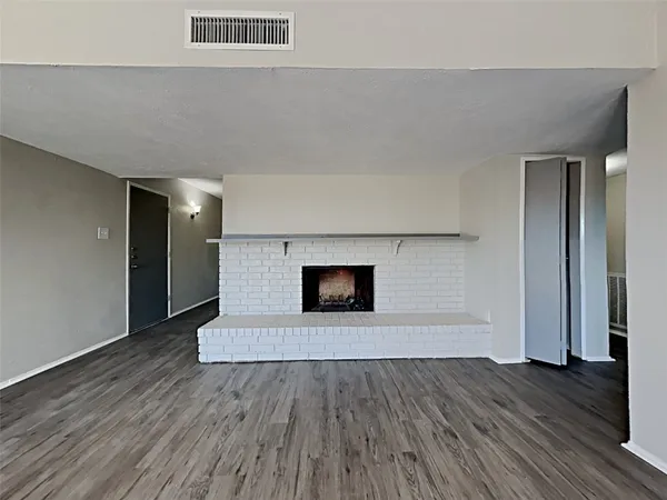 a view of an empty room with wooden floor and a fireplace