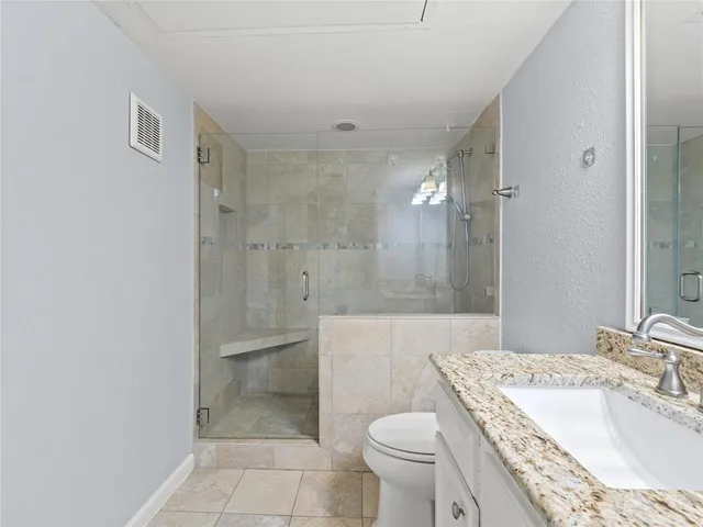 a bathroom with a granite countertop sink a toilet a mirror and shower