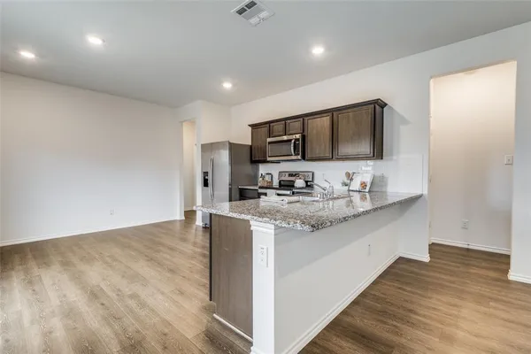 a view of kitchen with stainless steel appliances granite countertop a sink and a stove top oven with wooden floor