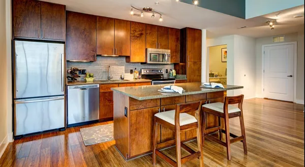 a kitchen with stainless steel appliances granite countertop a stove a refrigerator a sink a dining table and chairs with wooden floor