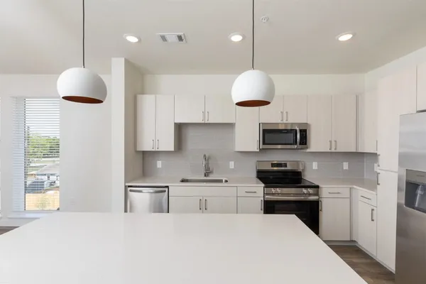 a kitchen with stainless steel appliances a stove a sink a microwave a refrigerator and white cabinets with wooden floor