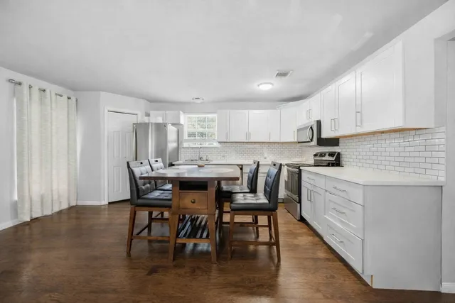 a kitchen with stainless steel appliances kitchen island granite countertop a table chairs sink and cabinets