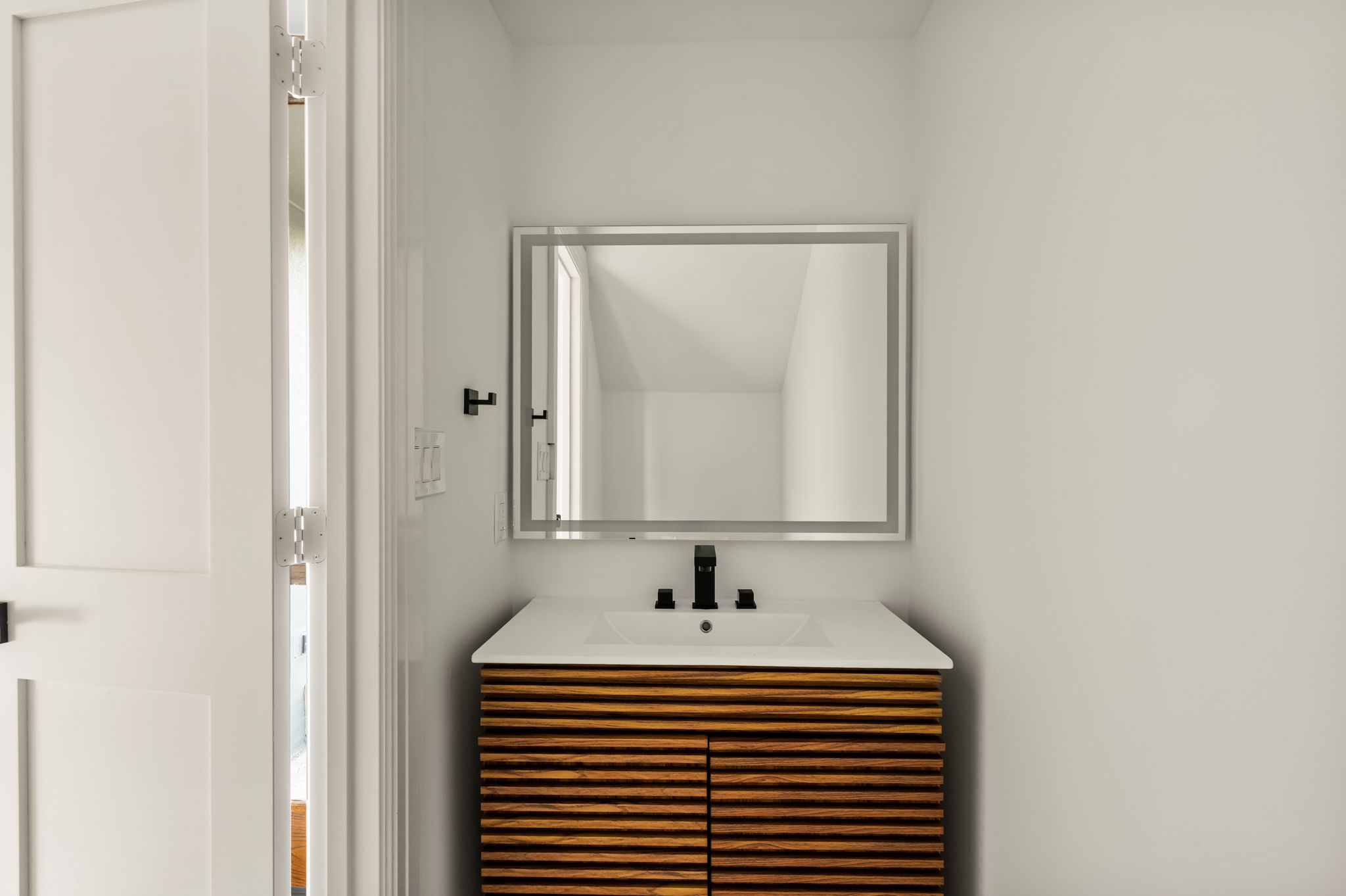 1111 West 12th Street, Unit 107 Austin, TX 78703 - Photo 37 of 38 Vanity featuring a slatted wood-finish cabinet, integrated sink, white countertop, and matte black faucet