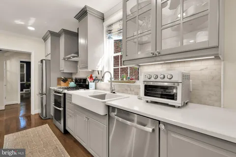 a kitchen with stainless steel appliances granite countertop a stove a sink a microwave a refrigerator and white cabinets with wooden floor