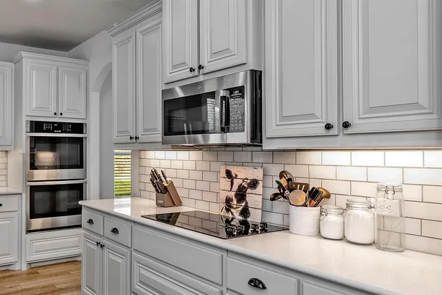 a large white kitchen with a sink a window and stainless steel appliances