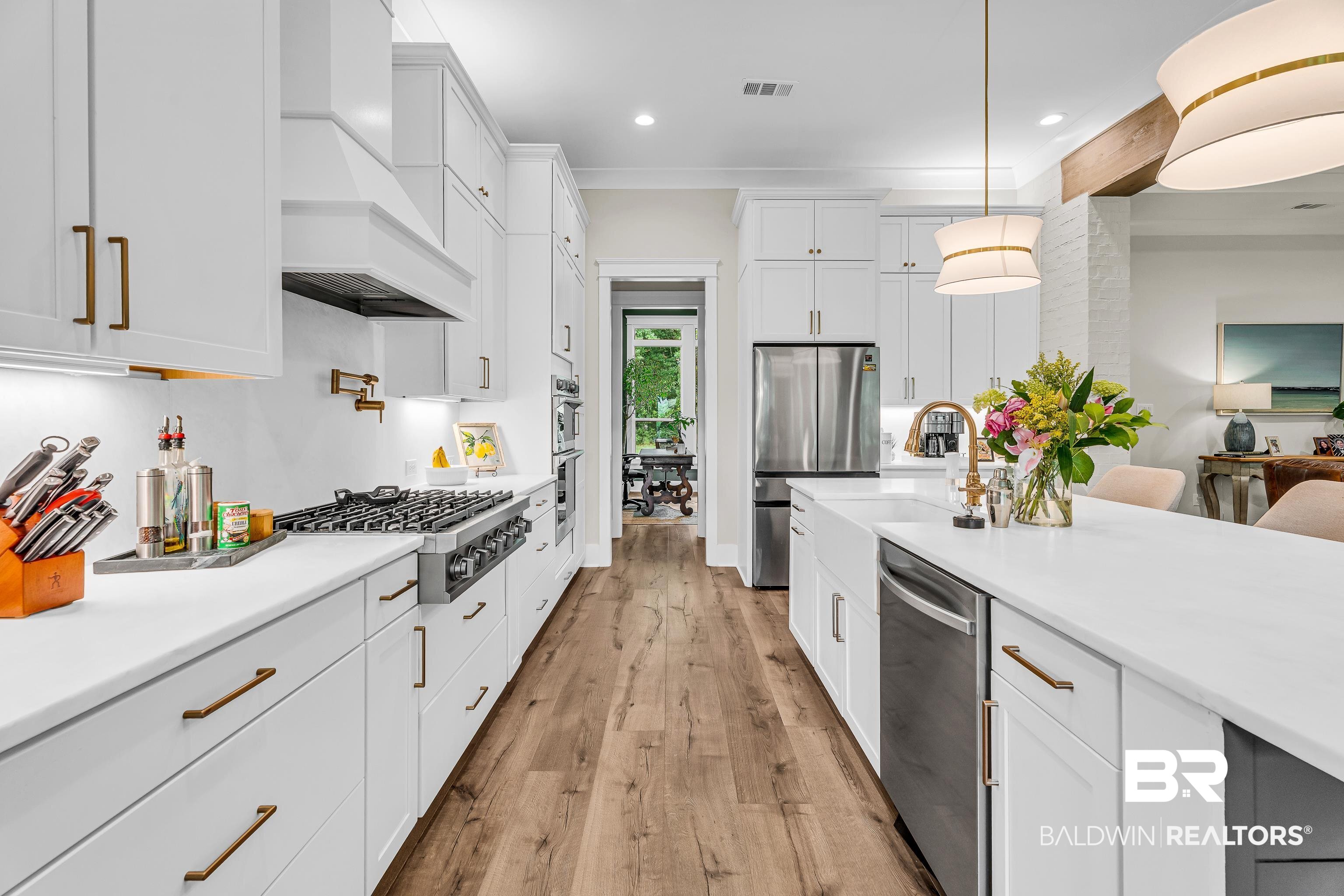 17541 Polo Ridge Boulevard Fairhope, AL 36532 - Photo 7 of 19 Well-appointed kitchen featuring extensive white cabinetry, brass hardware, wood-finish flooring, a stainless steel range with pot filler, and a large center island with a farmhouse sink