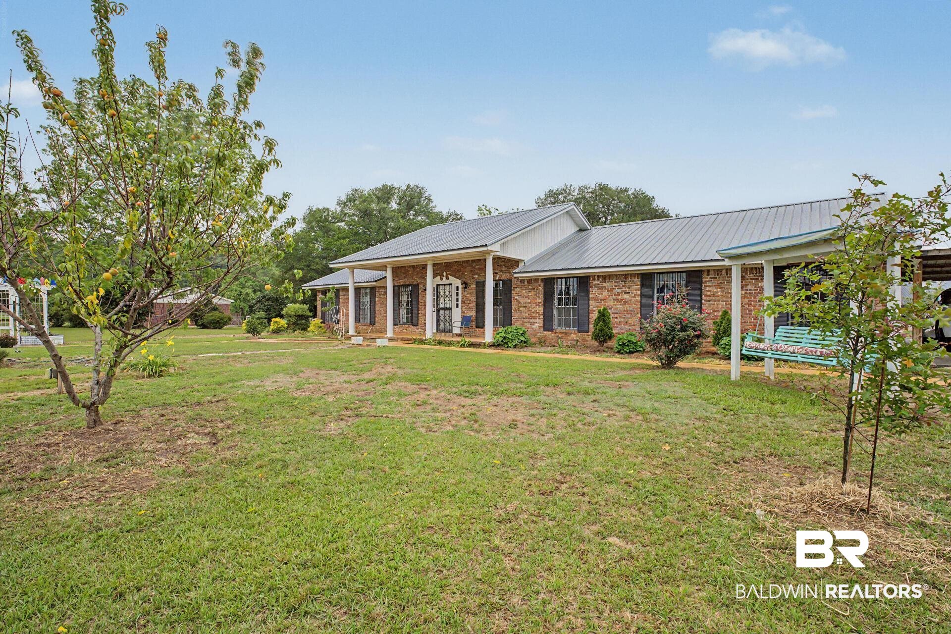 3791 Robinsonville Road Atmore, AL 36502 - Photo 11 of 47 Brick exterior home featuring a metal roof, covered front porch with white columns, and black louvered shutters