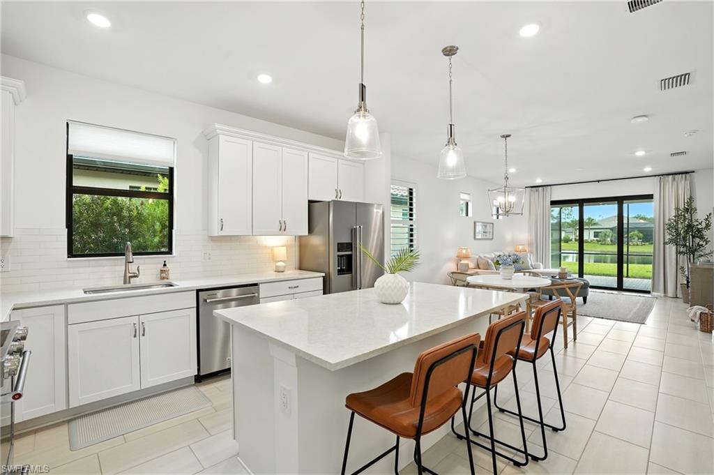 a kitchen with stainless steel appliances kitchen island a table chairs sink and cabinets