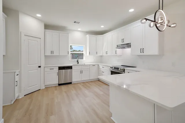a large white kitchen with cabinets a sink a window and stainless steel appliances