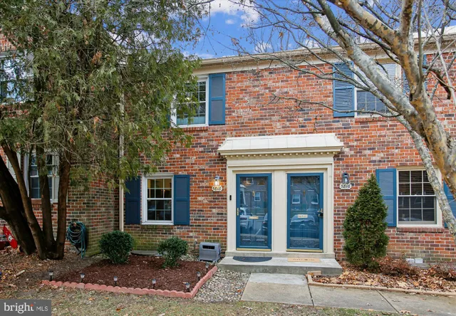 a view of a brick house with many windows plants and large tree
