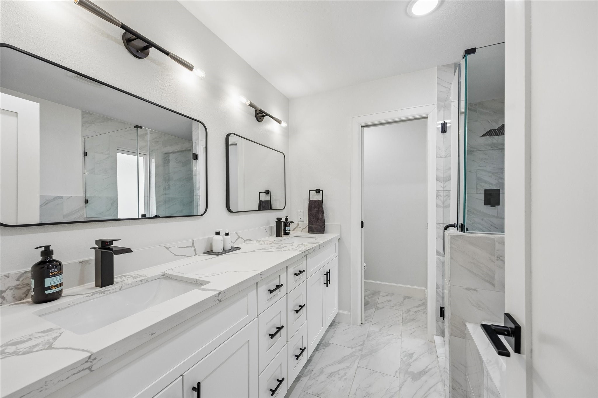 1420 Indiana Street Houston, TX 77006 - Photo 18 of 31 This bathroom features a modern design with dual sinks, elegant marble countertops, and sleek black fixtures. It includes large mirrors, ample cabinet storage, and a spacious glass-enclosed shower with contemporary tile work.