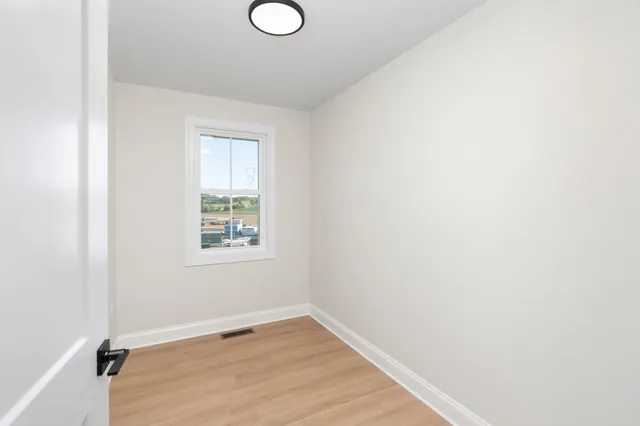 a view of an empty room with wooden floor and a window