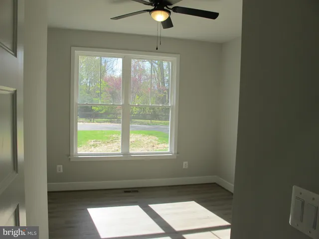 an empty room with wooden floor a ceiling fan and windows